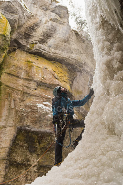 Альпинист зимой стоит у скалистой горы — стоковое фото