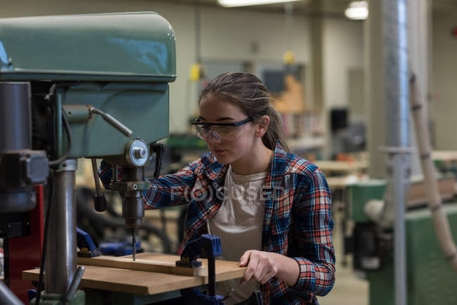 Female carpenter using vertical drill machine at workshop — Stock Photo