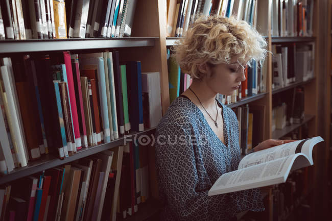 Jovem mulher lendo um livro na biblioteca — Fotografia de Stock