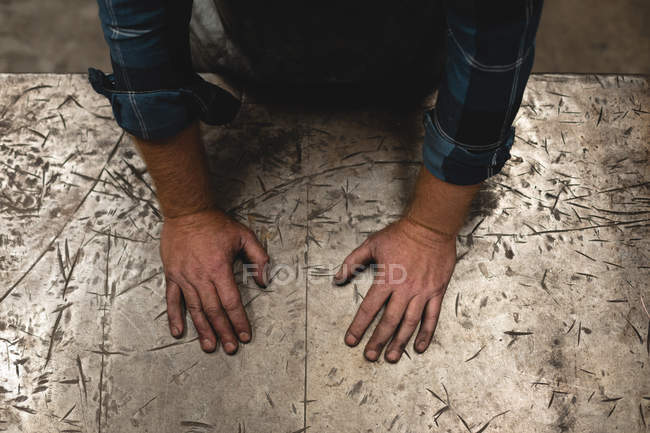 Schmied steht mit Händen auf Metalltisch in Werkstatt — Stockfoto