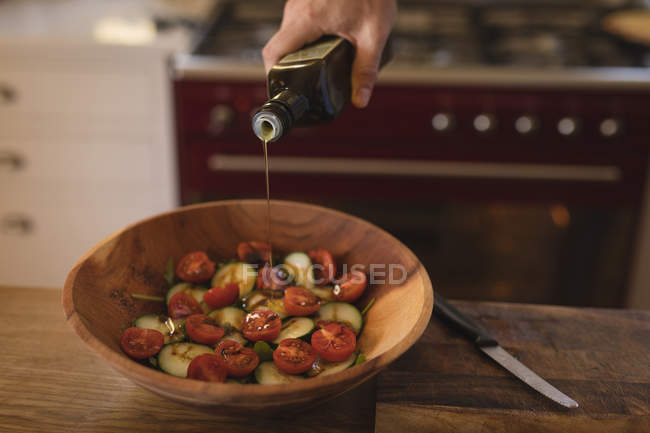 Мужчина наливает съедобное масло на овощи на кухне дома — стоковое фото