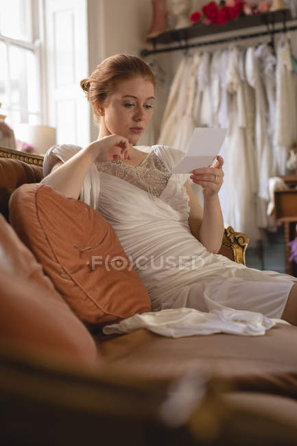 Jeune mariée en robe de mariée lisant une note à la boutique — Photo de stock