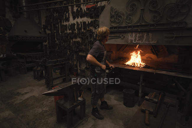 Кузнец нагревает металлический стержень в огне в мастерской — стоковое фото