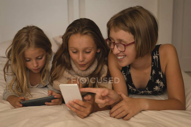 Frères et sœurs utilisant le téléphone portable dans la chambre à coucher à la maison — Photo de stock