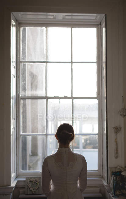Mariée en robe blanche regardant par la fenêtre à la boutique, vue arrière — Photo de stock