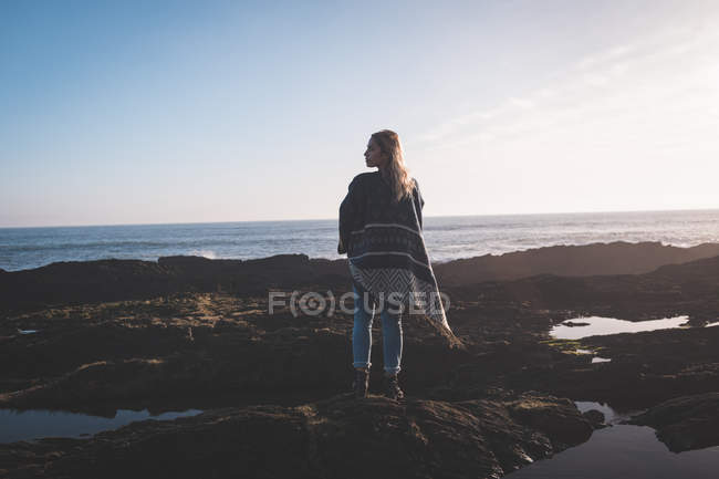 Vue arrière d'une femme debout sur un rocher sur une plage — Photo de stock