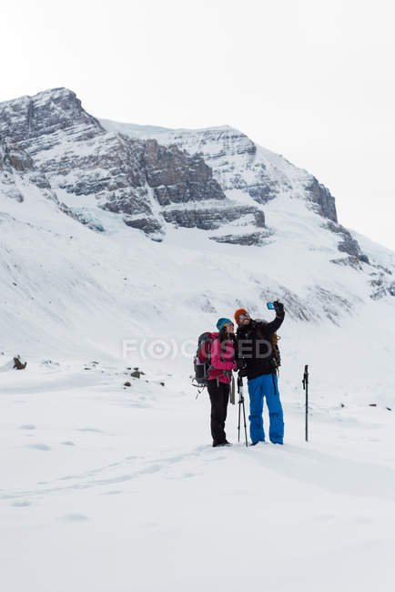 Couple taking selfie with mobile phone on a snow covered mountain during winter — Stock Photo