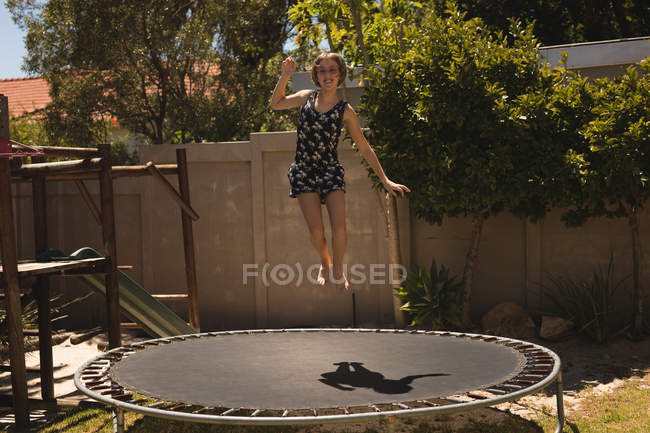 Fille sautant sur un trampoline dans le jardin par une journée ensoleillée — Photo de stock