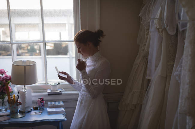 Novia joven en vestido de novia leyendo una nota en la boutique - foto de stock
