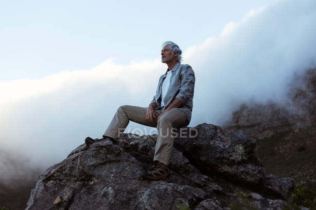 Senderista mayor sentado en una roca en el campo - foto de stock