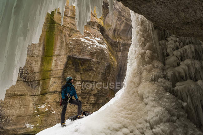 Hombre escalador de pie cerca de la montaña de hielo rocoso durante el invierno - foto de stock