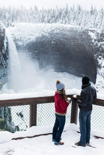Couple in warm clothing looking at waterfall during winter — Stock Photo