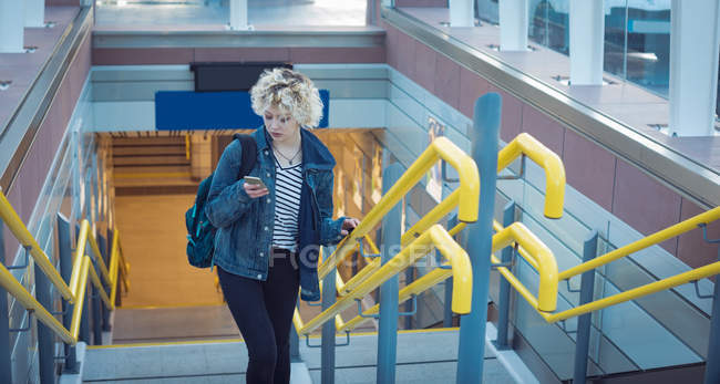 Young woman using mobile phone while moving upstairs — Stock Photo