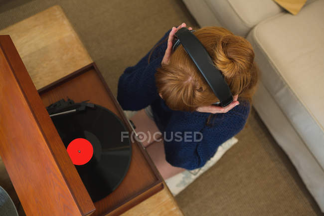 Жінка в навушниках слухає музику на грамофоні вдома — стокове фото
