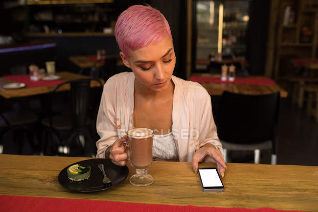 Stilvolle Frau benutzt Handy beim Schoko-Milchshake im Restaurant — Stockfoto