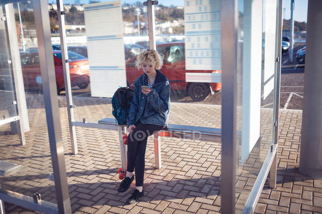 Mulher usando telefone celular na parada de ônibus em um dia ensolarado — Fotografia de Stock