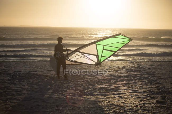 Hombre surfista de pie con cometa en la playa al atardecer - foto de stock