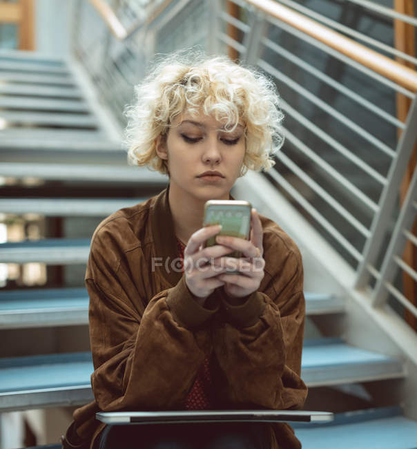 Молодая женщина использует мобильный телефон на лестнице — стоковое фото