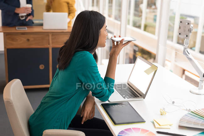 Female graphic designer talking on mobile phone in office — Stock Photo