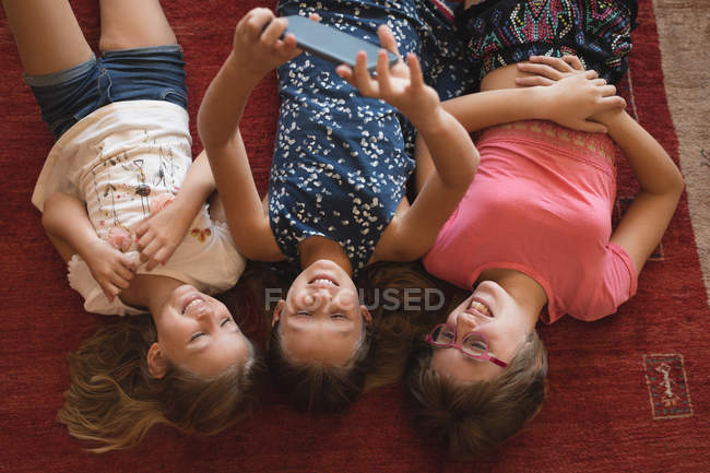 Frères et sœurs prenant selfie avec téléphone portable dans le salon à la maison — Photo de stock