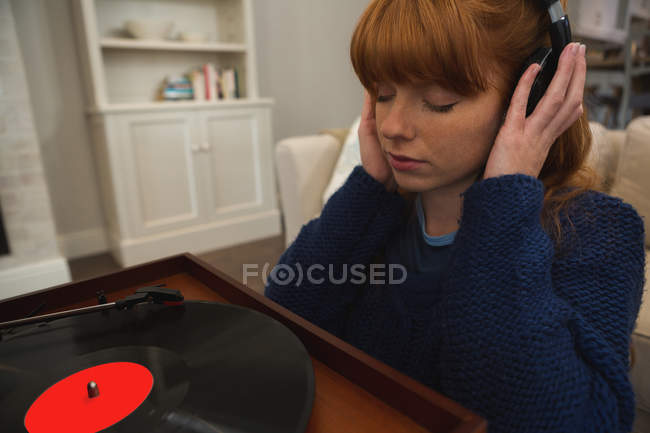 Woman in headphones listening to music on gramophone at home — Stock Photo