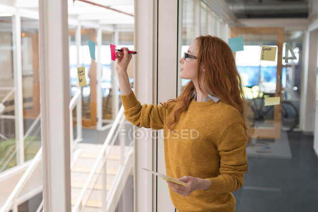 Young female executive writing on sticky notes in office — Stock Photo
