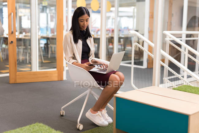 Female executive using laptop and digital tablet in office — Stock Photo