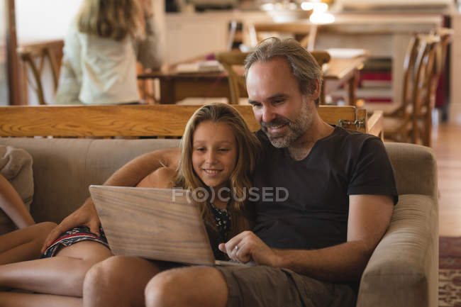 Padre e hija usando el ordenador portátil en la sala de estar en casa - foto de stock