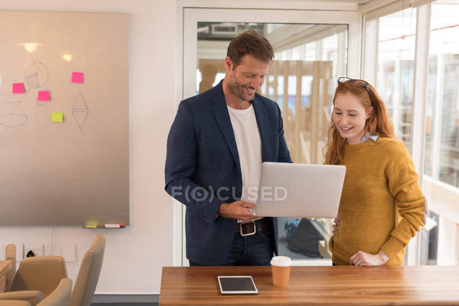 Compañeros de negocios felices discutiendo sobre portátil en la oficina - foto de stock