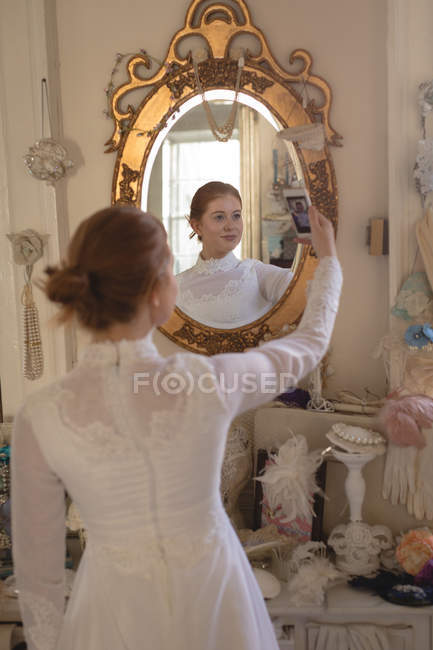 Caucasian bride taking selfie with mobile phone in boutique at mirror — Stock Photo