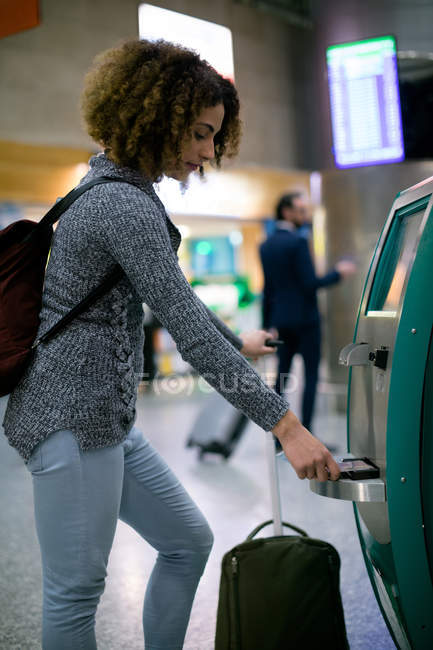 Mujer usando la máquina de billetes de avión en el aeropuerto - foto de stock
