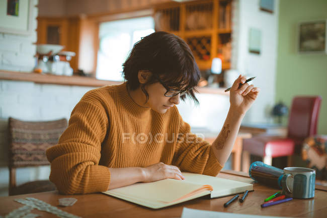 Mujer dibujando un boceto en un libro en casa - foto de stock