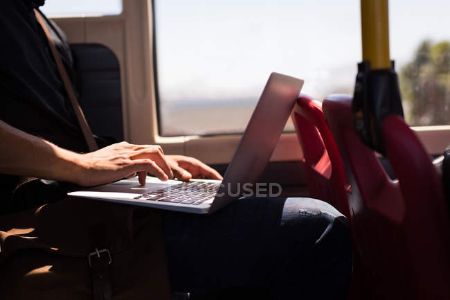 Sección media del hombre de negocios que usa la computadora portátil mientras viaja en autobús - foto de stock