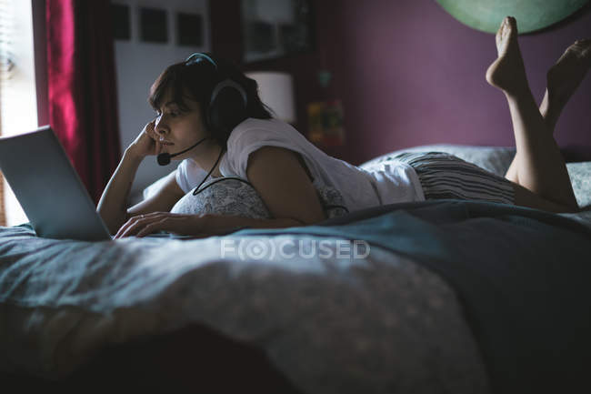 Жінка використовує ноутбук з гарнітурою в спальні вдома — стокове фото