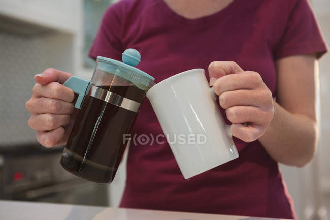 Seção média de mulher derramando café preto em caneca na cozinha em casa — Fotografia de Stock