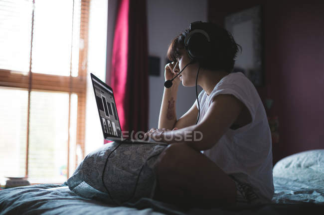 Женщина с ноутбуком с гарнитурой в спальне на дому — стоковое фото