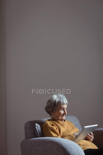 Donna anziana che utilizza tablet digitale in soggiorno a casa — Foto stock