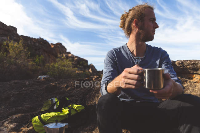 Senderista masculino tomando café en el campo en un día soleado - foto de stock