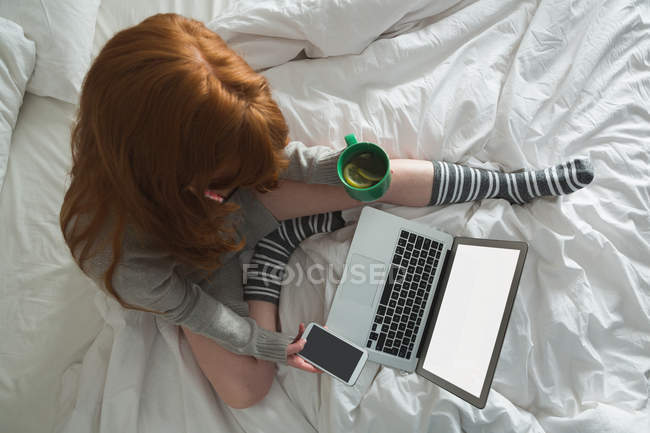 Femme utilisant un téléphone portable dans la chambre à coucher à la maison — Photo de stock