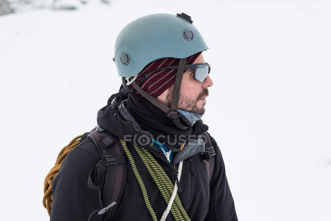 Pensativo montañero macho de pie con casco y gafas de sol en una región nevada - foto de stock