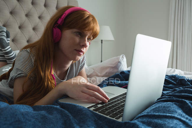 Жінка використовує ноутбук з навушниками в спальні вдома — стокове фото