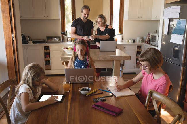 Les parents utilisent un ordinateur portable pendant que les enfants étudient dans la cuisine à la maison — Photo de stock