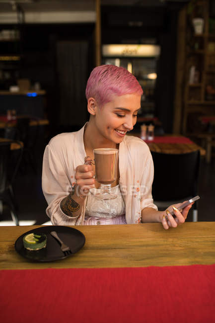 Femme élégante utilisant un téléphone mobile tout en ayant milk-shake au chocolat au restaurant — Photo de stock
