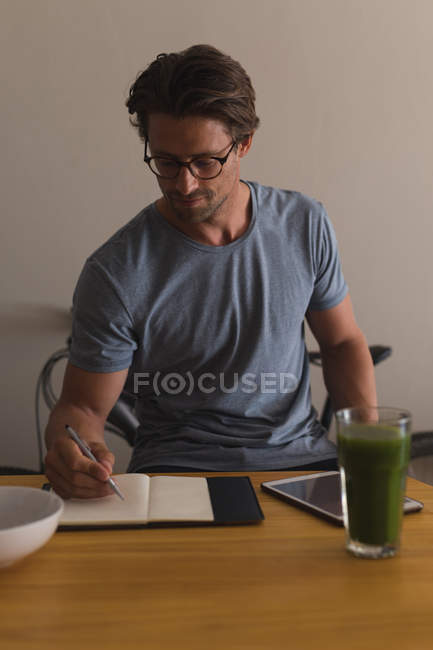 Hombre escribiendo en un diario en la sala de estar en casa - foto de stock