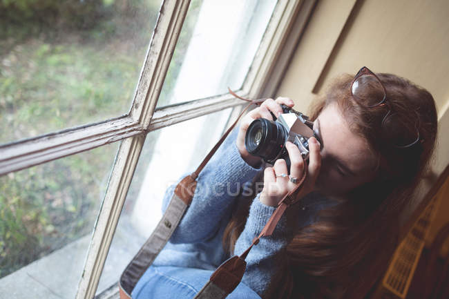Mujer tomando fotos con cámara retro cerca de la ventana en casa - foto de stock