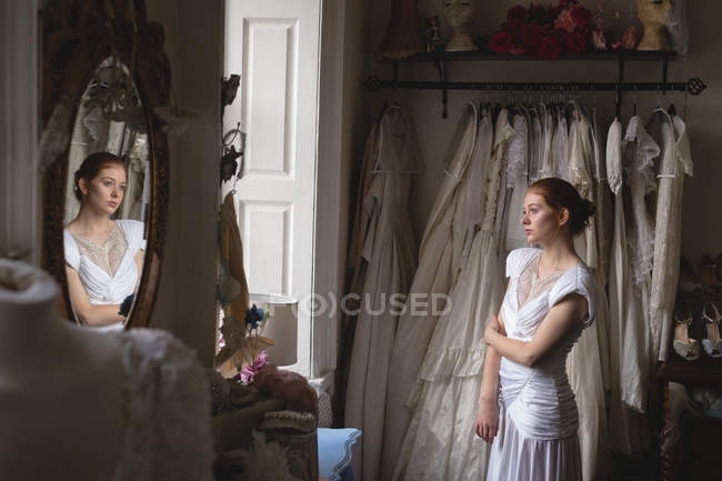Young bride in wedding dress standing near window — Stock Photo