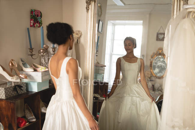 Молодая невеста в свадебном платье смотрит в зеркало в бутике — стоковое фото