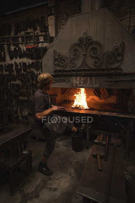 Кузнец нагревает металлический стержень в огне в мастерской — стоковое фото