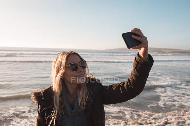 Женщина делает селфи с мобильного телефона на пляже в солнечный день — стоковое фото