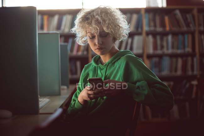 Jeune femme utilisant un téléphone portable dans la bibliothèque — Photo de stock